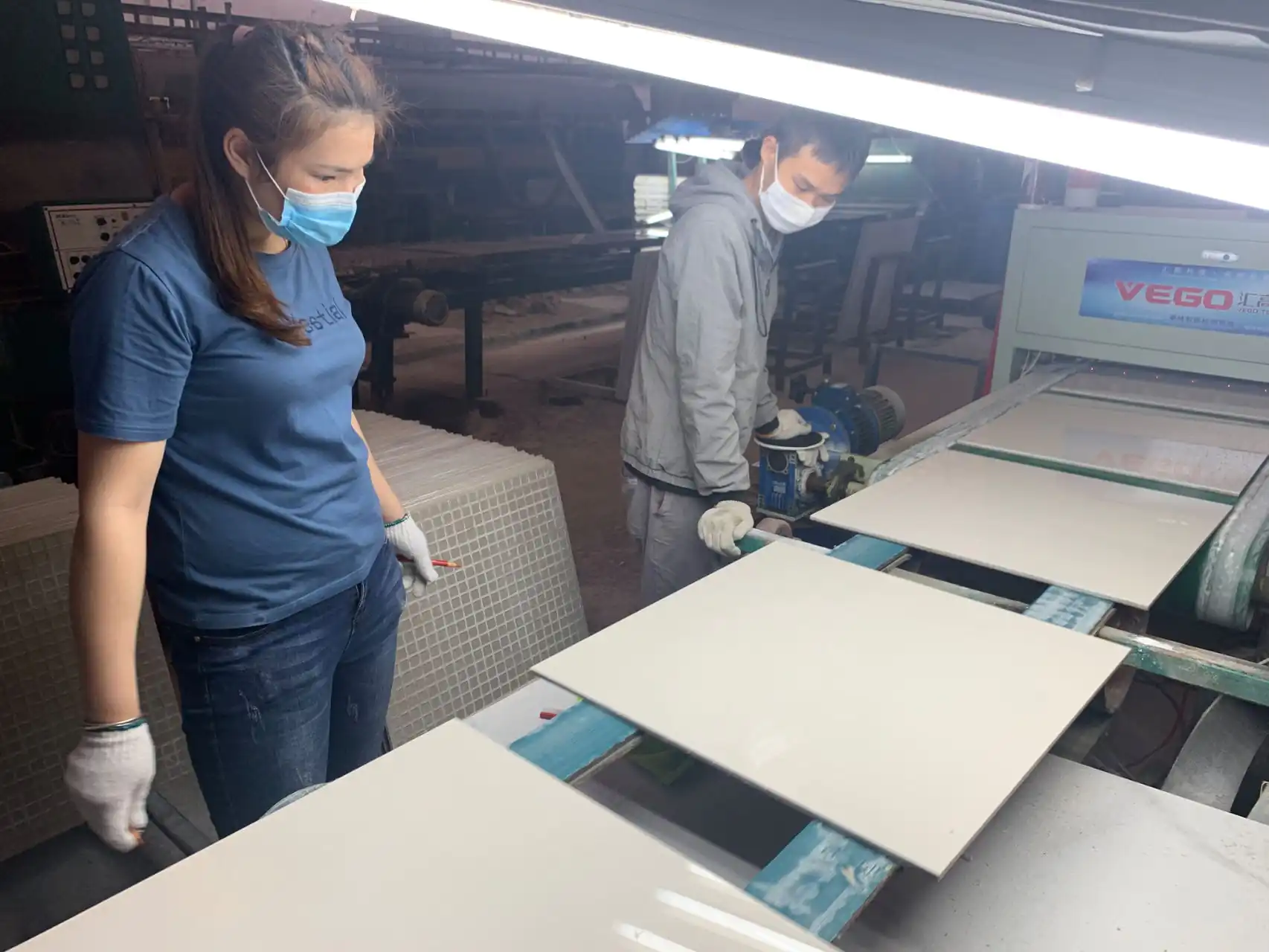 Factory workers inspect polished tiles under light, ensuring flawless surface